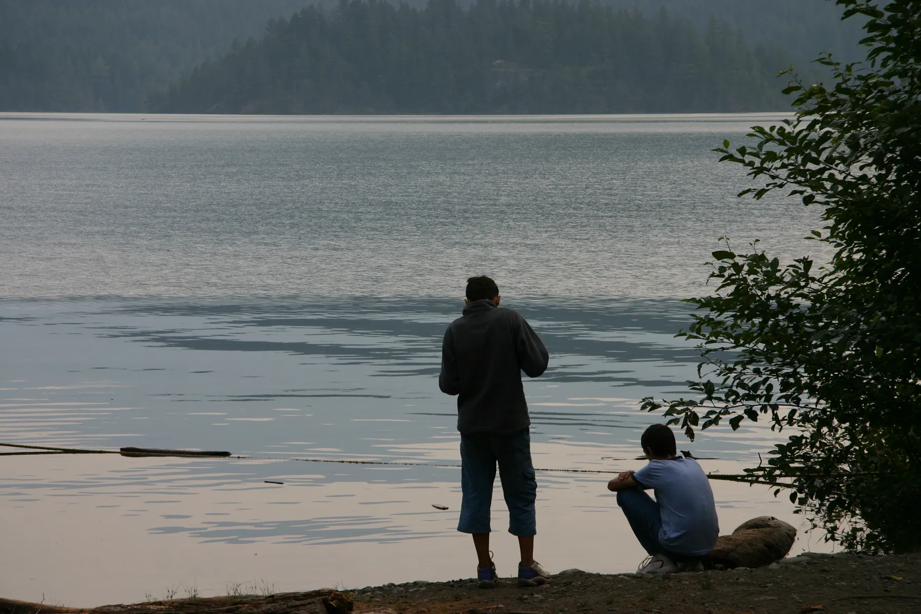 A man and a young man at the water's edge, looking out